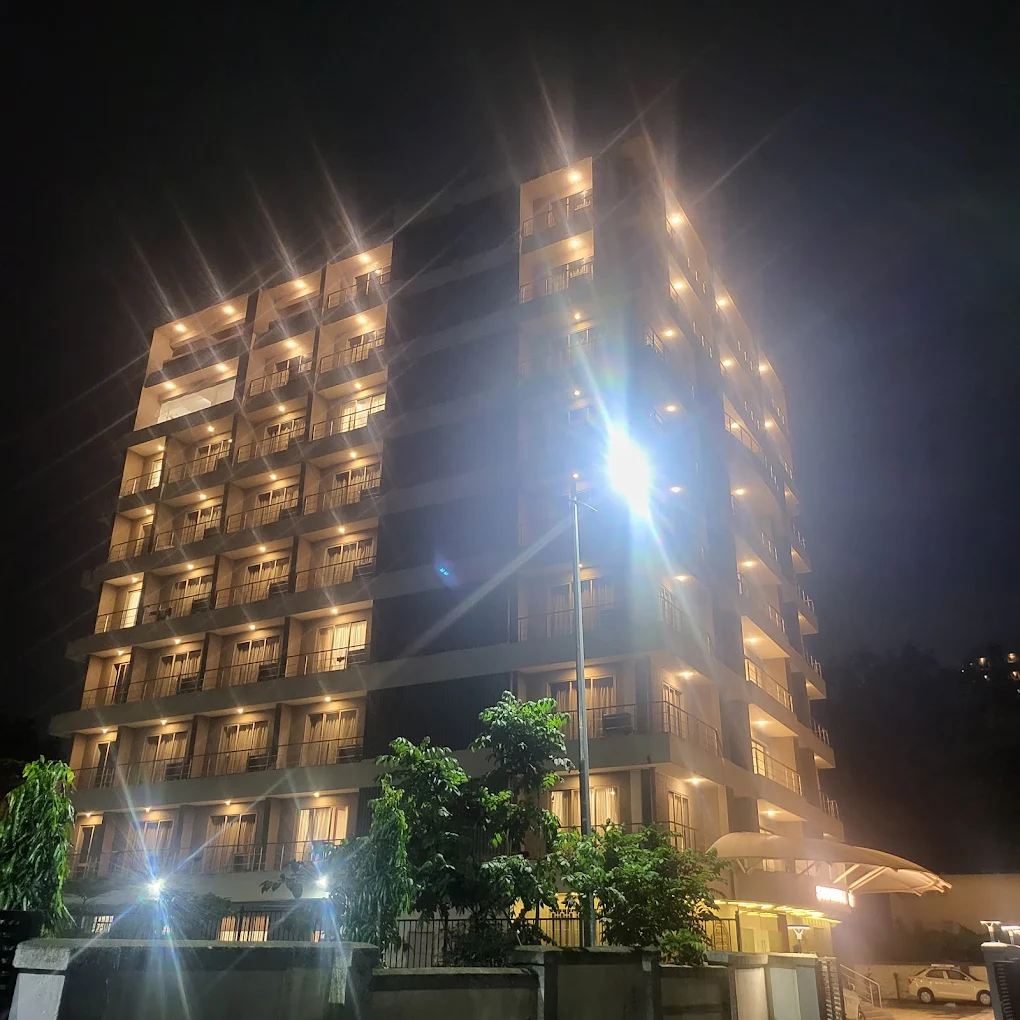 A brightly lit, spacious suite with a king-sized bed, a separate living area, and large windows overlooking a cityscape, showcasing the luxury accommodation at Hotel Swamiraj.