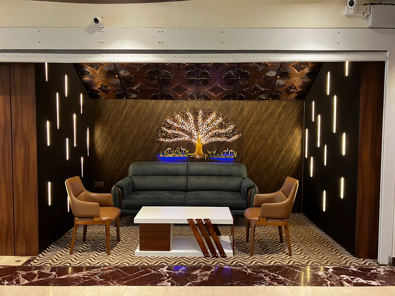 A photograph of a Hotel Swamiraj Suite, featuring a separate living area with comfortable seating, a dining table, and a well-equipped kitchenette. The decor is modern and stylish.