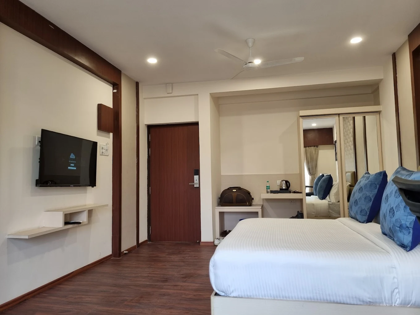 A photograph of a Hotel Swamiraj Standard Room, showcasing a comfortable queen-size bed, a work desk, and a cozy atmosphere. The room is clean and well-maintained.